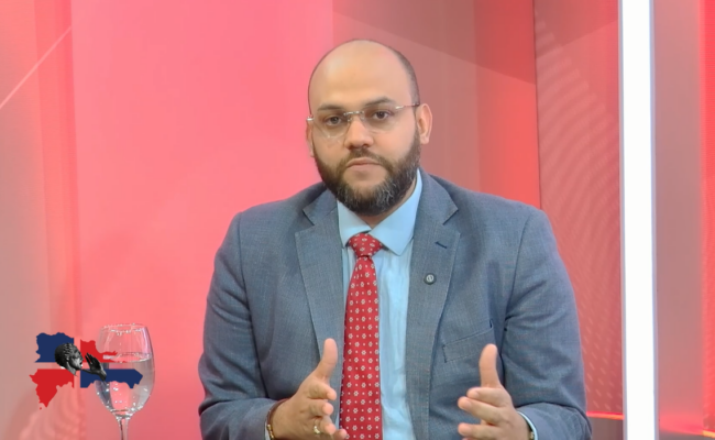 Hombre, blanco con traje habla frente a la cámara.